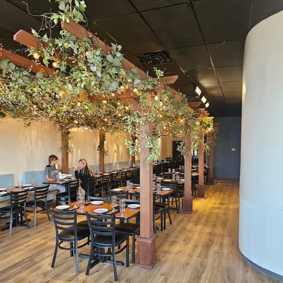 Roti Indian Kitchen dining room with wooden pergolas, string lights, and two people dining.