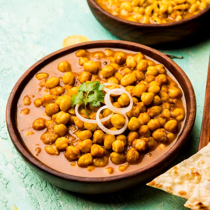 Roti Indian Kitchen's chole bhature, a chickpea curry garnished with onions and cilantro, served with naan.