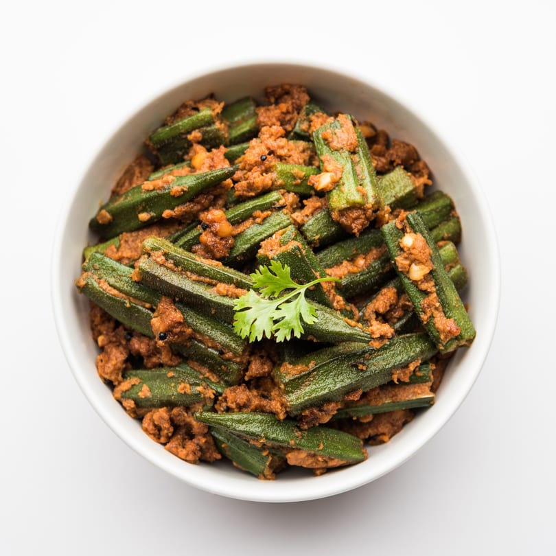 A white bowl filled with Indian-style okra, coated in a rich, reddish-brown spice mixture, garnished with cilantro.