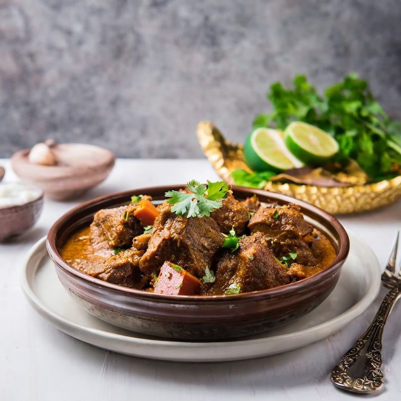 Roti Indian Kitchen's rich brown curry with meat and vegetables, garnished with cilantro and lime.